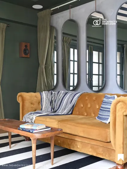 A cozy media room with a mustard yellow tufted sofa, striped rug, and a wall of mirrors to create an illusion of space.