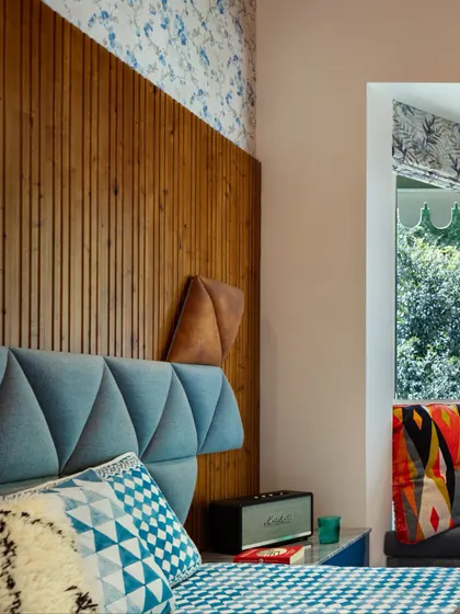 A close-up of the geometric upholstered headboard and fluted wood paneling in the kids' room. The mix of patterns and textures, from the checkered bedspread to the floral wallpaper, sparks joy and youthful energy.