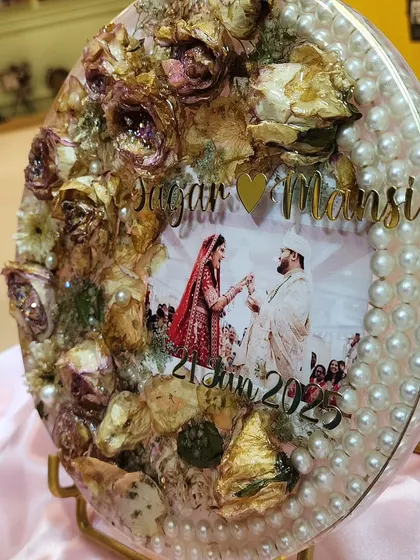 This oval resin frame is a beautiful example of how I can preserve your wedding varmala. I arranged the dried roses and other flowers around the couple's photo and added a border of pearls to create a classic, elegant look. It’s a wonderful centerpiece for a side table.