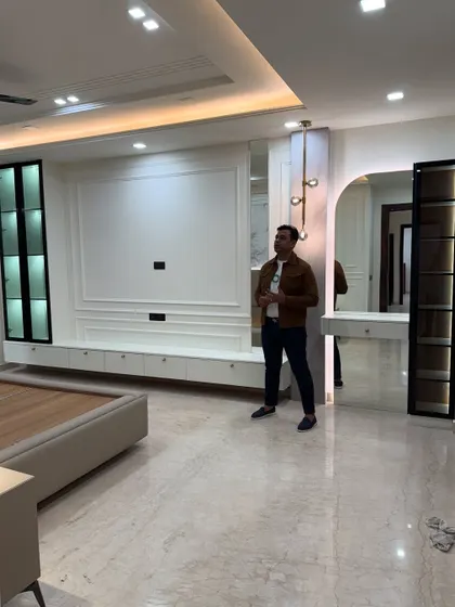 A wide view of a master bedroom nearing completion. The space includes a large TV unit, a built-in dressing table with an arched mirror, and elegant display cabinets.