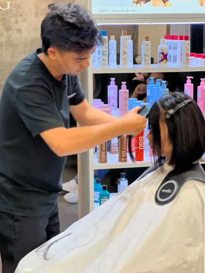 A stylist carefully cutting bangs, with our professional product display in the background.