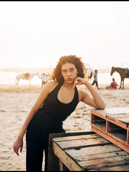 A relaxed pose using a wooden pallet as a prop. The background shows the life of the beach, adding an authentic, candid feel to this fashion shot.