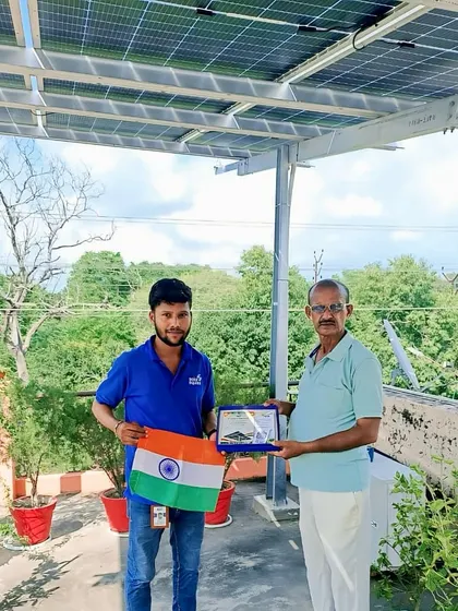 A happy customer and our team member pose with the Indian flag and a certificate of installation.