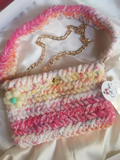 A multi-color pink and cream crochet sling bag with a gold chain strap, perfect for a unique, bohemian look.