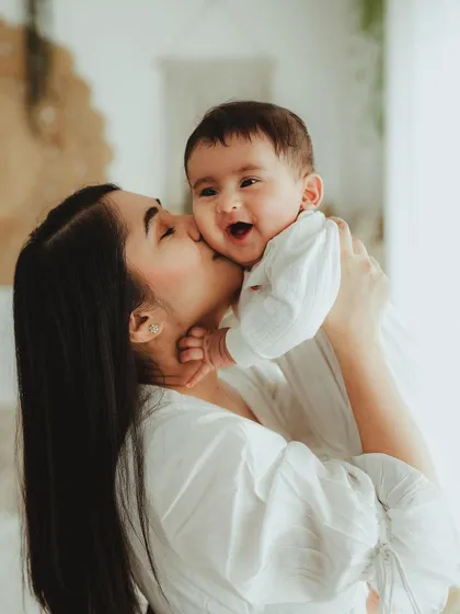 A mother kissing her laughing baby's cheek. This image is full of genuine happiness and maternal love.