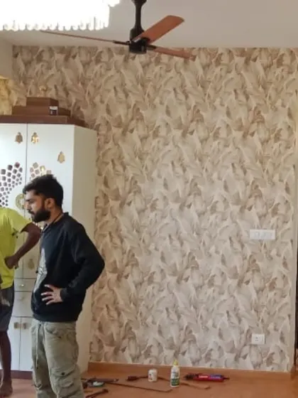 An installation in progress, showing a large wall being covered with a neutral-toned leaf pattern wallpaper. You can see my team at work, ensuring a perfect application.
