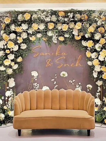 A dreamy engagement stage for Sanika and Sneh, featuring a beautiful arch of white and yellow roses against a soft grey backdrop. The personalized names and delicate floral details create a romantic and welcoming atmosphere.