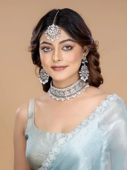 A complete view of a silver-toned bridal set with a maang tikka, choker, and earrings, styled with a light blue saree for a modern bridal look.