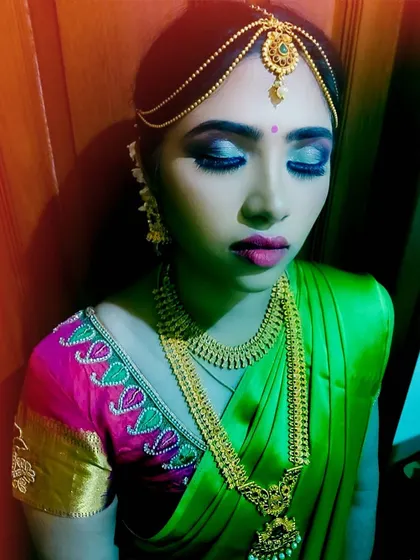 A detailed shot of a South Indian bridal or festive look. The focus is on the dramatic blue and silver smokey eye, paired with a pink lip, traditional gold jewelry, and a matha patti hair accessory.