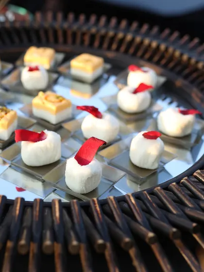 An elegant tray of assorted Indian sweets. We present traditional mithai with a modern flair, using mirrored trays and delicate garnishes like rose petals to elevate the experience.