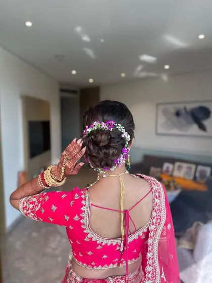 This beautiful floral bun is created with a mix of purple and white flowers to match the bride's pink lehenga. It's a soft, romantic updo perfect for a wedding ceremony.