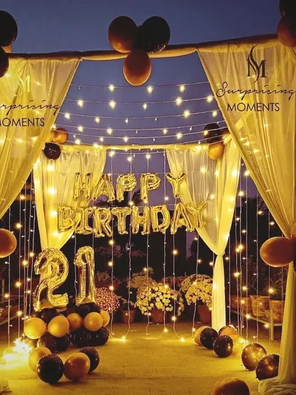 A stunning terrace transformation for a 21st birthday. I created a canopy with drapes and fairy lights, adding 'Happy Birthday' foil balloons and light-up numbers for a perfect outdoor party ambiance.