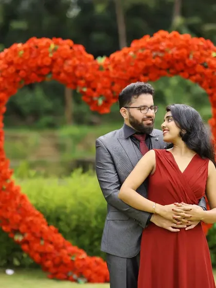 A classic romantic pre-wedding photo, with the couple embracing in front of a large heart made of red flowers.