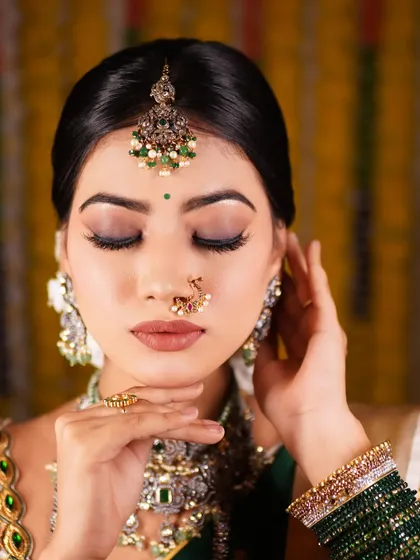 A close-up of a flawless reception makeup look. The focus is on beautifully blended eyeshadow and a perfect base, complemented by a traditional nose ring and maang tikka.