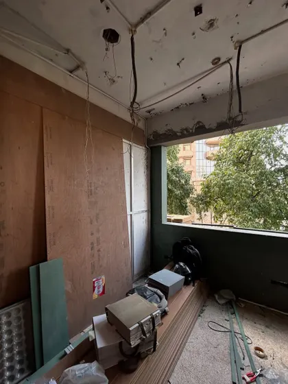 Plywood sheets and construction materials are stacked and ready as a room begins to take shape, with a large window framing the green world outside.