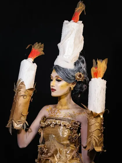 A profile view of the candle look, highlighting the sculptural elements of the costume and headpiece.