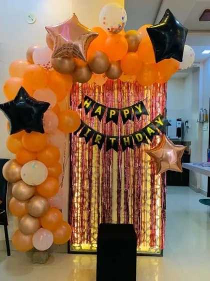 A simple yet stylish birthday photo corner. An orange, black, and rose gold balloon arch frames a shimmering fringe backdrop, perfect for taking party pictures.