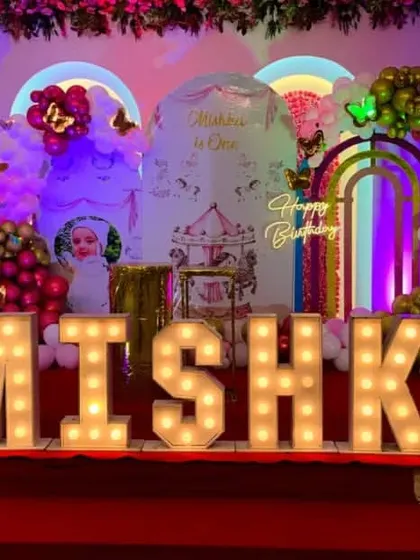 A whimsical carousel and butterfly theme for Mishka's first birthday. The grand stage setup features large light-up letters, a custom backdrop, and colorful balloon decorations.