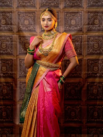 A stunning full-length portrait of a bride in a pink and gold silk saree. This showcases the complete look, including the intricate hairstyle, makeup, and perfect saree drape.