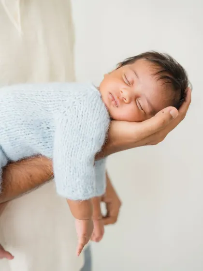 A newborn rests peacefully in their father's hand, a pose that shows just how tiny and precious they are.