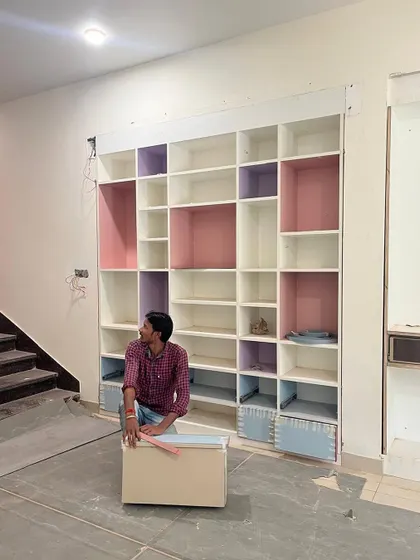 A custom shelving unit in progress. The design incorporates a playful color-blocking scheme with pastel pink, purple, and blue cubbies, creating a functional and visually interesting storage solution.