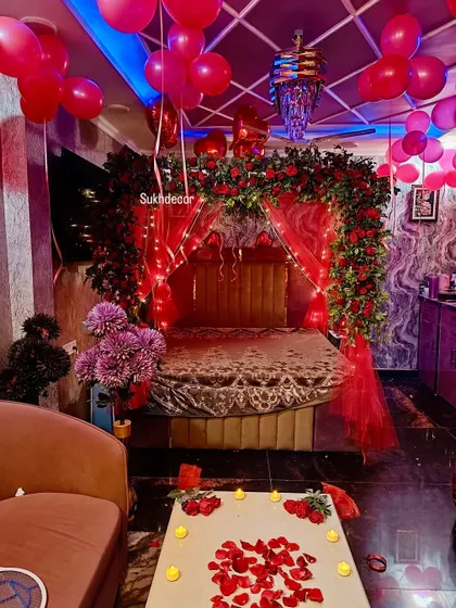 A slightly different angle of the romantic room, showing the relationship between the decorated bed, the floating balloons, and the candlelit table in the foreground.