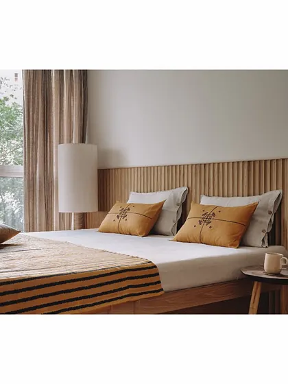 The mother's bedroom in the 'Sand' project features a hand-carved oak wood headboard. We also designed a totem-like floor lamp from leftover plywood on site, turning waste material into a beautiful, functional art piece.