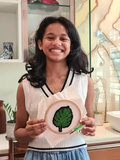 A young participant beaming with pride over her finished green leaf punch needle art.