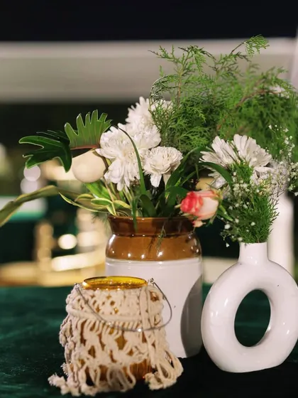 A close-up of a modern centerpiece with fresh flowers and a macrame-covered candle holder, part of a chic Mehendi night setup.