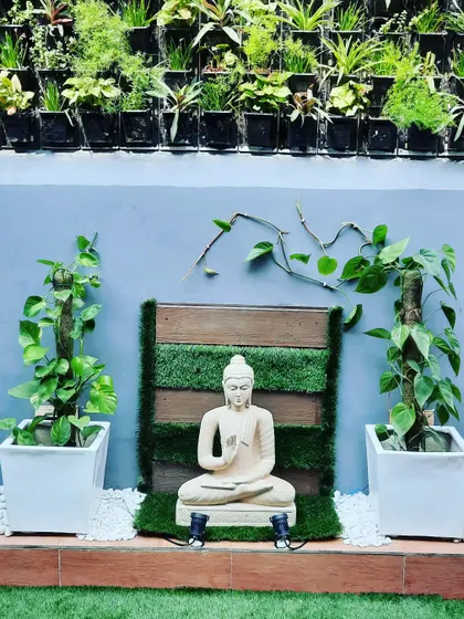 A close-up of the serene Buddha statue set against a wood and grass backdrop, with a full vertical garden above.