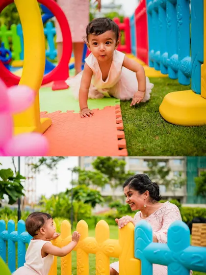 A baby girl explores a colorful play area at her birthday party, sharing a sweet moment with her mother over the fence.