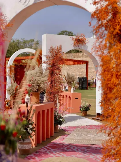 An inviting entrance to the rust-orange Haldi, with a pathway through modern arches and decor elements that blend rustic textures with a contemporary color palette.