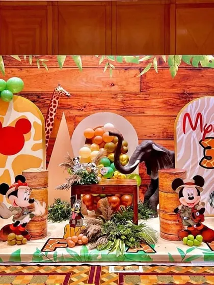 Welcome to a Mickey Mouse jungle safari adventure! This expansive backdrop brings the wild indoors with a wood-paneled wall, lush balloon garlands in earthy tones, and beloved characters like Mickey and Pluto ready for exploration. It's a perfect example of how I transform a space into a story.