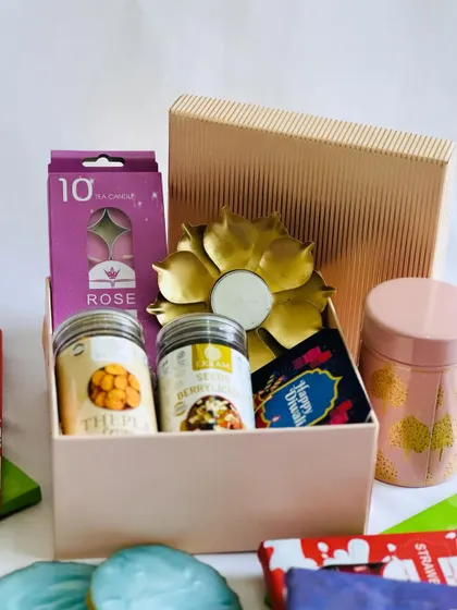 A lovely pastel pink gift box for Diwali, containing scented candles, dry fruit jars, and a lotus diya.