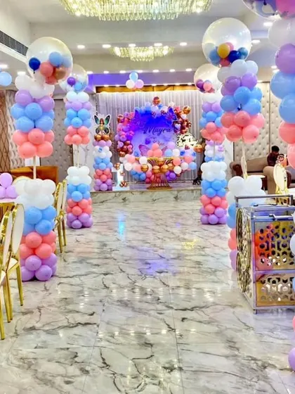 A beautiful butterfly-themed party in a large hall. The aisle is lined with pastel-colored balloon pillars, leading to a stunning stage backdrop, creating a grand and enchanting pathway for the birthday girl and guests.