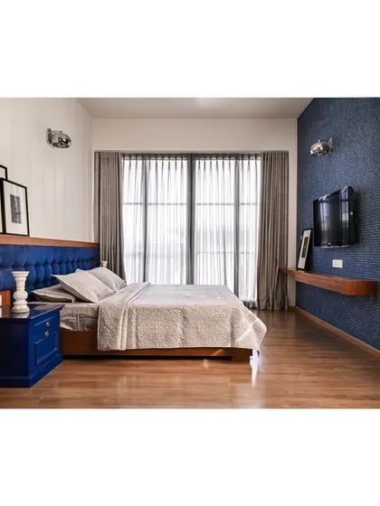 The master suite in "Anchorage 162" uses a deep blue color palette, with a tufted velvet headboard and a textured wallpaper to create a lavish, comfortable feel.