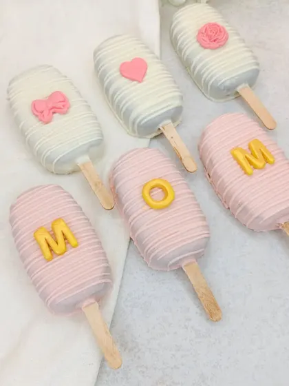 Our "MOM" cakesicles, decorated in pink and white chocolate, are a cute and delicious part of our Mother's Day hamper.