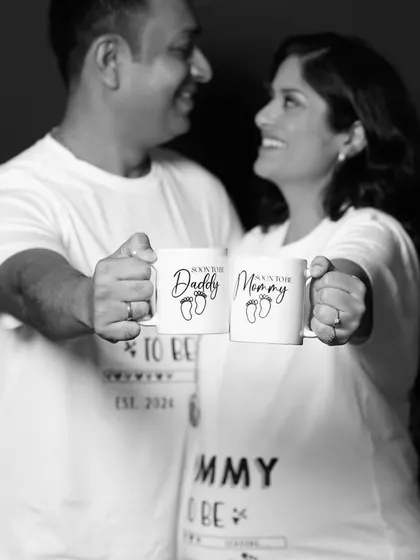 A creative black and white shot focusing on "Daddy to be" and "Mommy to be" mugs held by the couple. Props like these add a fun, personalized element to the photoshoot.
