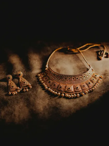 An elegant flat-lay of the bride's traditional gold necklace and earrings. The dramatic lighting highlights the exquisite craftsmanship of the jewelry, an essential part of the bridal ensemble.