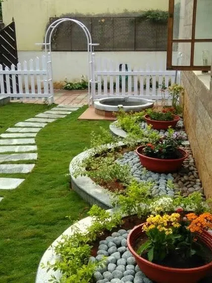 This garden features curved flowerbeds filled with colorful flowers and river pebbles, contrasting beautifully with the green lawn and stone pathway.