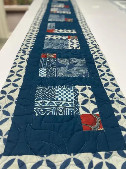 A close-up of the indigo table runner, showing the different block-printed patterns and the leaf-shaped quilting.