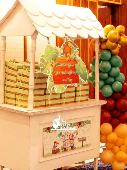 A themed cart for party favors, decorated with a jungle-print sign that reads 'Thank you for swinging on by', adding a fun, punny touch to the celebration.