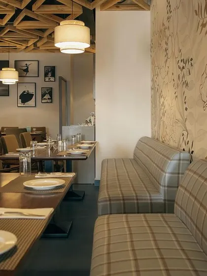A view of the dining area, showing the combination of the hand-painted mural and plaid banquette seating. This juxtaposition of artistic flair and traditional pattern adds depth and character to the restaurant's interior.