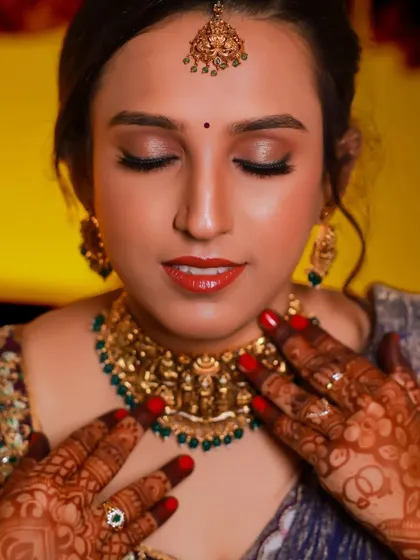 A beautiful close-up of the bride, focusing on her intricate henna and traditional temple jewelry necklace.