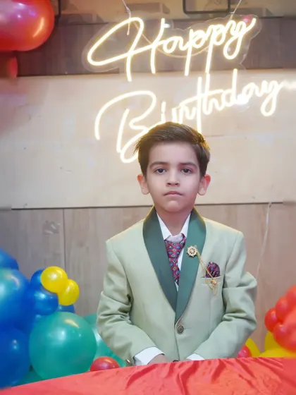 A solo portrait of the birthday boy looking dapper in his suit in front of a 'Happy Birthday' neon sign.