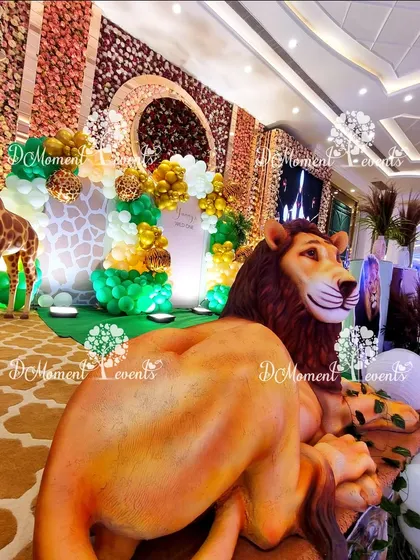 A close-up shot from behind a large lion prop, giving a unique perspective of the detailed jungle stage and its giraffe and balloon elements.