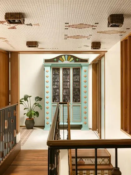 A wider view of the upper landing, showing the mosaic-tiled ceiling, the custom balustrade with turned-wood elements, and the colorful bar cabinet.