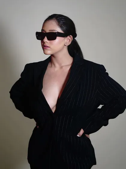 This side profile with hands on hips emphasizes the oversized fit of the pinstripe blazer. It's a power pose that sells not just a product, but a feeling of confidence.