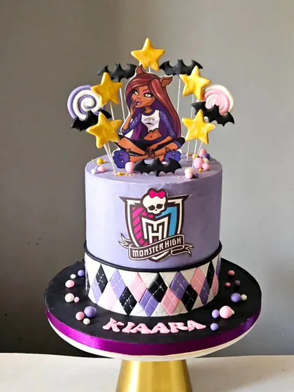 A Monster High School themed cake. This two-tier design features a purple and black color scheme, an argyle pattern, and a character topper for a cool and spooky vibe.