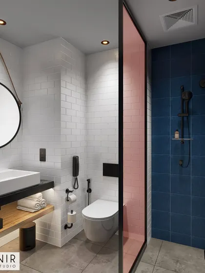 A compact and modern hotel bathroom. The design uses a combination of white subway tiles and bold blue tiles, separated by a pink glass panel, to create a visually interesting space.